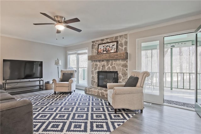 living room featuring a stone fireplace, wood finished floors, ceiling fan, and ornamental molding