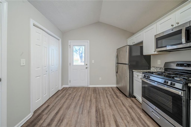 kitchen with white cabinetry, stainless steel appliances, light stone counters, light hardwood / wood-style floors, and vaulted ceiling