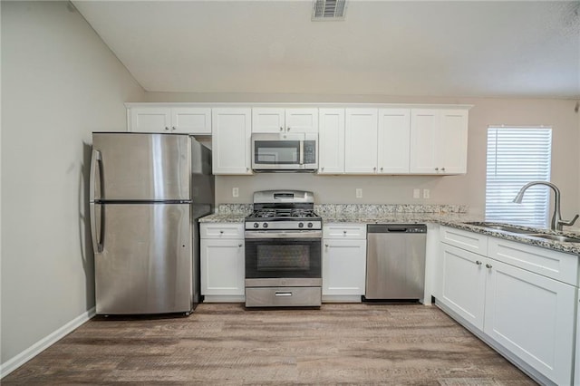 kitchen featuring sink, white cabinets, stainless steel appliances, light stone countertops, and light hardwood / wood-style flooring