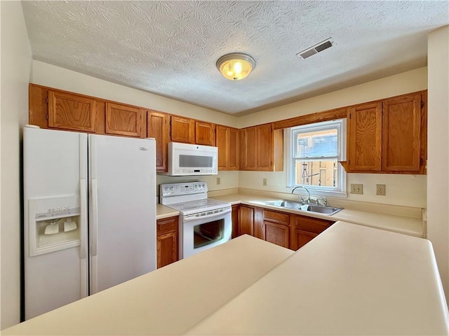 kitchen featuring brown cabinets, white appliances, visible vents, and a sink