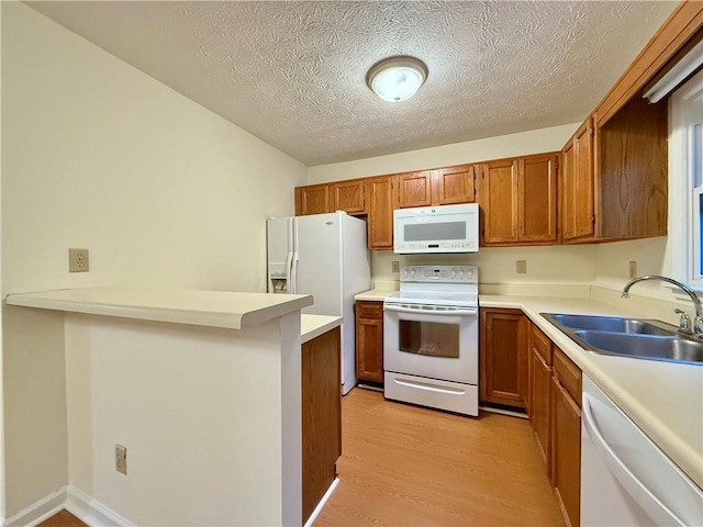 kitchen with white appliances, brown cabinets, light countertops, light wood-style floors, and a sink