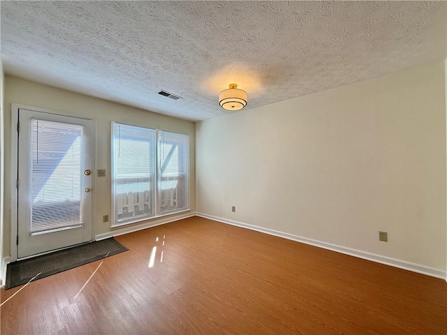 interior space featuring baseboards, a textured ceiling, visible vents, and wood finished floors