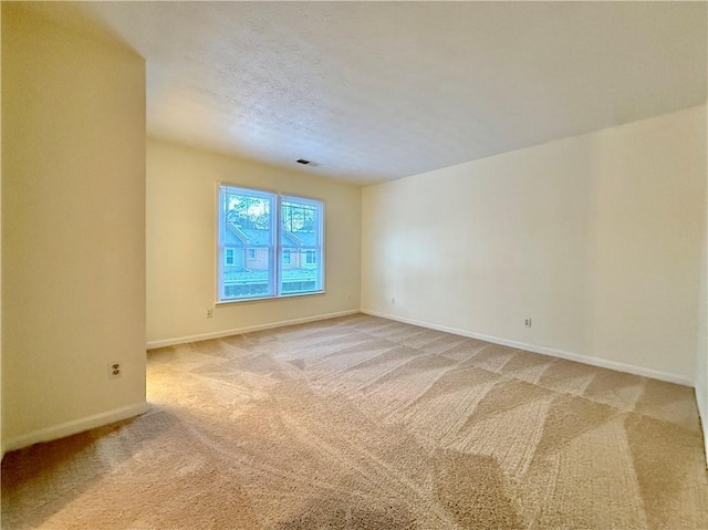 empty room with light colored carpet, visible vents, baseboards, and a textured ceiling