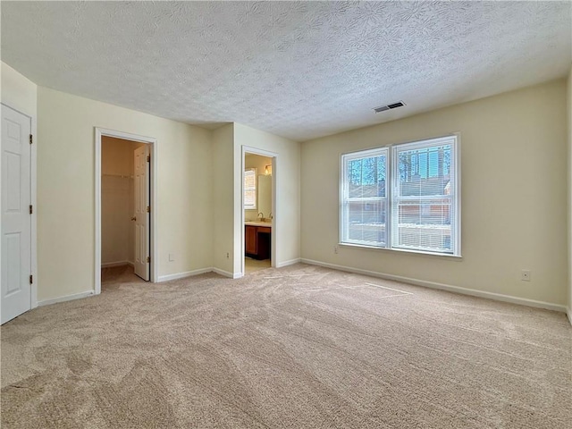 unfurnished bedroom with baseboards, a walk in closet, visible vents, and light colored carpet