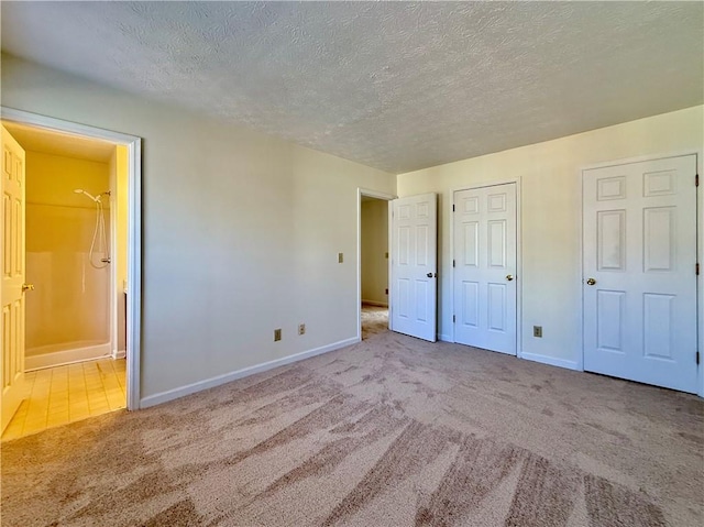 unfurnished bedroom with a textured ceiling, ensuite bath, carpet flooring, and baseboards