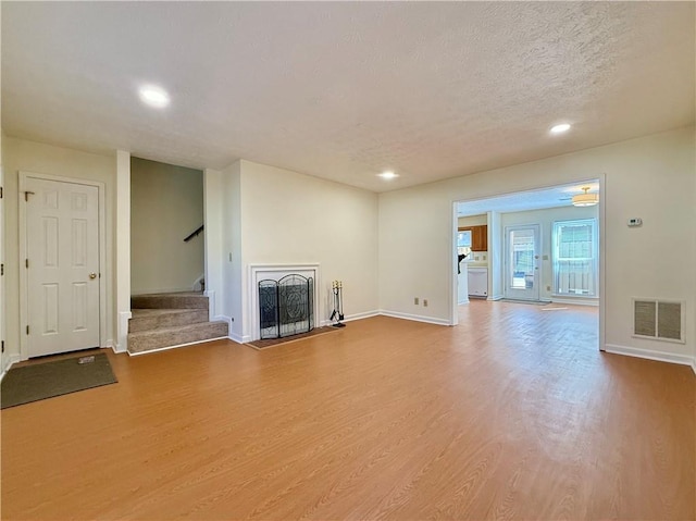 unfurnished living room with visible vents, a textured ceiling, wood finished floors, stairway, and a fireplace