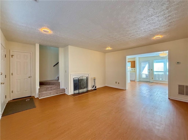 unfurnished living room featuring a fireplace with raised hearth, a textured ceiling, wood finished floors, visible vents, and stairs