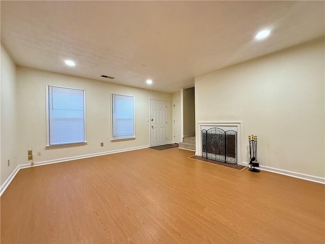 unfurnished living room with a fireplace, wood finished floors, visible vents, and baseboards