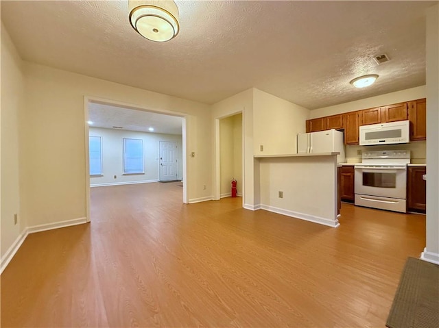 kitchen featuring a textured ceiling, white appliances, wood finished floors, open floor plan, and light countertops