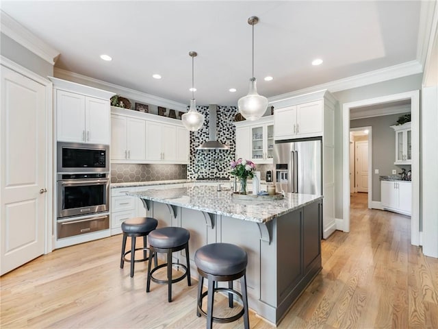 kitchen with pendant lighting, white cabinetry, a kitchen island with sink, stainless steel appliances, and wall chimney exhaust hood