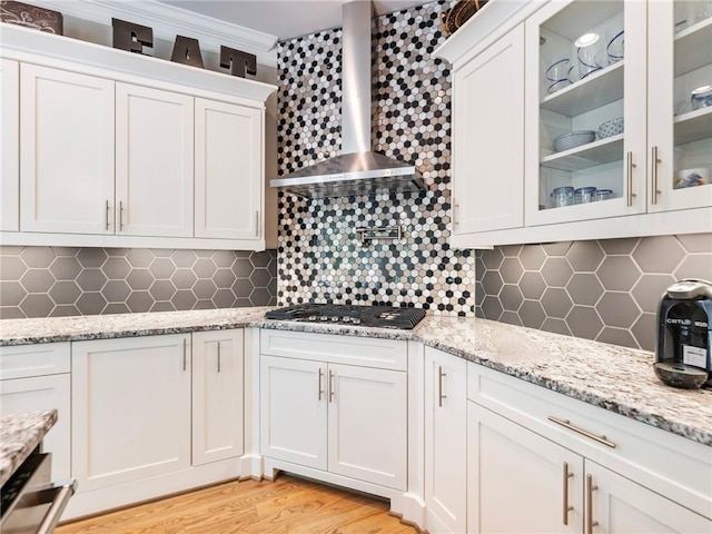 kitchen with tasteful backsplash, wall chimney exhaust hood, stainless steel gas cooktop, and white cabinets