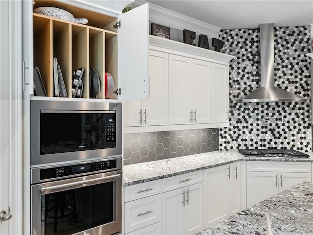 kitchen with wall chimney range hood, decorative backsplash, stainless steel appliances, and white cabinets