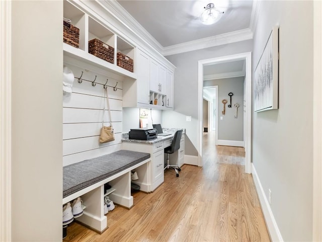 mudroom with crown molding, built in desk, and light wood-type flooring