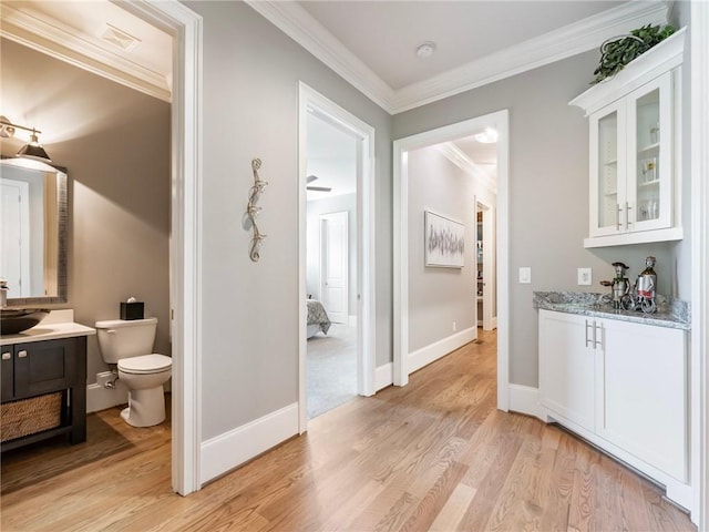 interior space with sink, white cabinets, light stone counters, crown molding, and light wood-type flooring