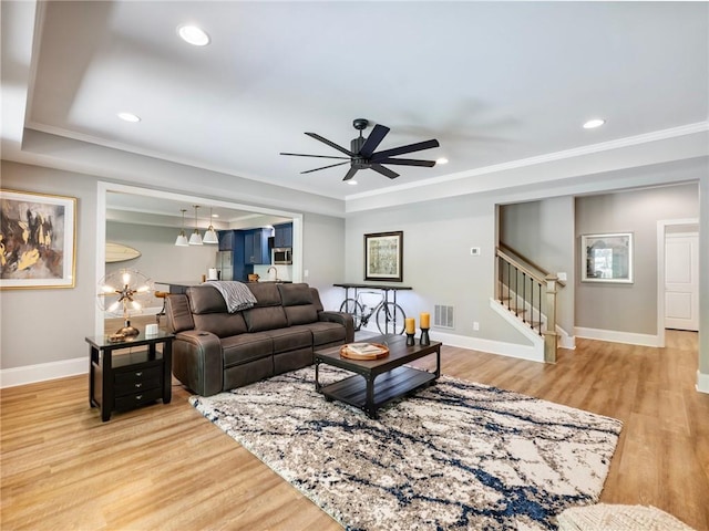 living room with crown molding, ceiling fan, a raised ceiling, and light wood-type flooring