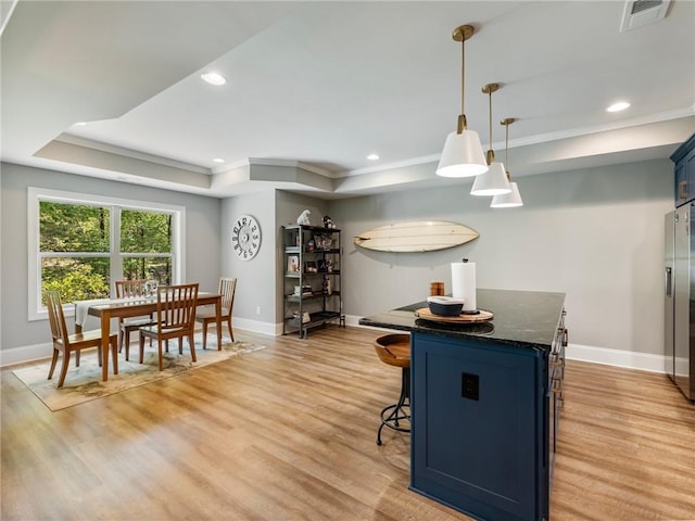 kitchen featuring blue cabinets, dark stone countertops, hanging light fixtures, light hardwood / wood-style floors, and a tray ceiling