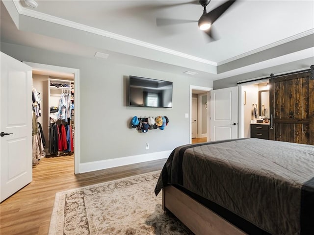 bedroom with a raised ceiling, ornamental molding, a barn door, and a walk in closet