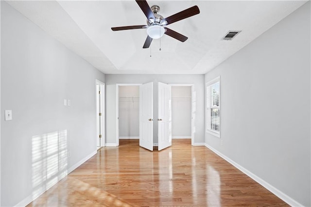 spare room with a tray ceiling, ceiling fan, and light wood-type flooring