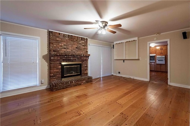 unfurnished living room with hardwood / wood-style flooring, a brick fireplace, ceiling fan, and ornamental molding