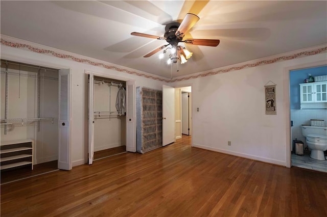 unfurnished bedroom featuring hardwood / wood-style floors, ensuite bathroom, two closets, and ceiling fan