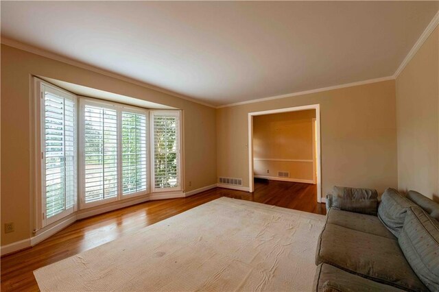 unfurnished living room featuring wood-type flooring and ornamental molding