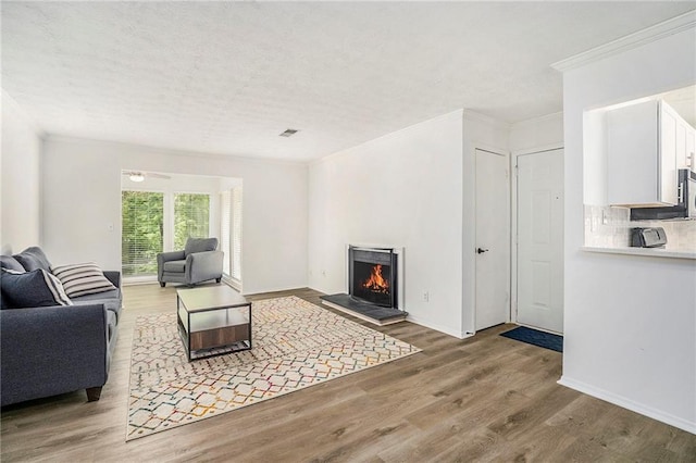 living area with crown molding, a lit fireplace, wood finished floors, and baseboards