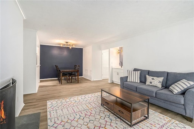 living room with light wood-type flooring, a chandelier, baseboards, and ornamental molding