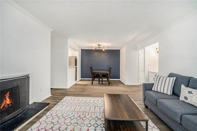 living room with a warm lit fireplace, wood finished floors, crown molding, a chandelier, and baseboards
