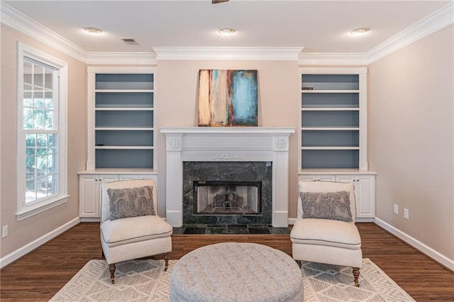 living area featuring crown molding, a fireplace, dark hardwood / wood-style flooring, and built in features