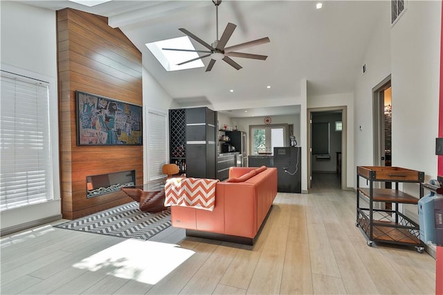 living room featuring light hardwood / wood-style flooring, lofted ceiling with skylight, and ceiling fan