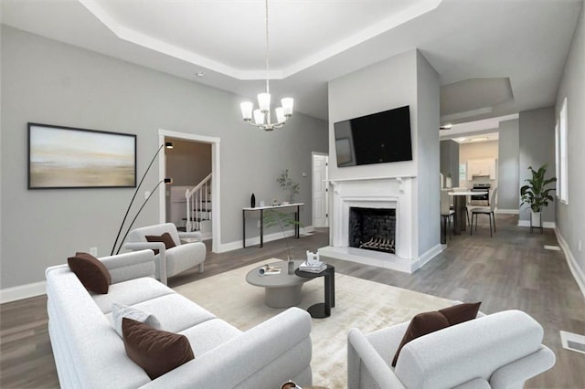 living room featuring a raised ceiling, wood-type flooring, and an inviting chandelier