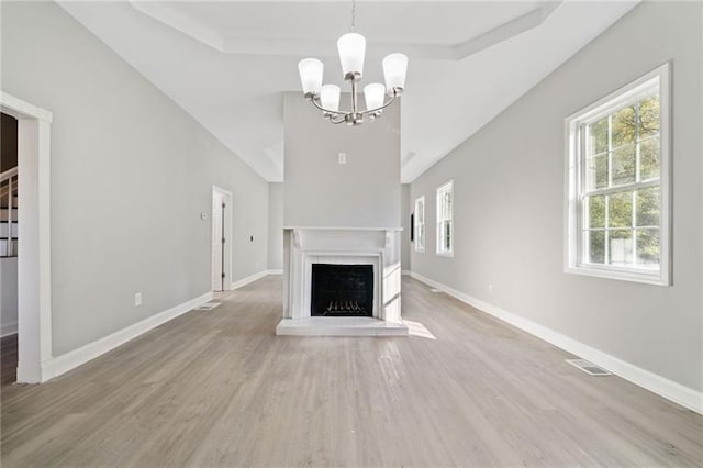 unfurnished living room with a tray ceiling, light hardwood / wood-style flooring, and a notable chandelier