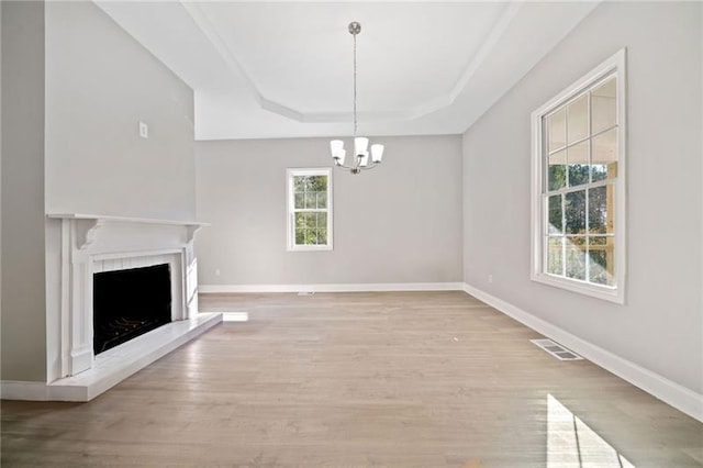 unfurnished living room with an inviting chandelier, a tray ceiling, and light hardwood / wood-style floors