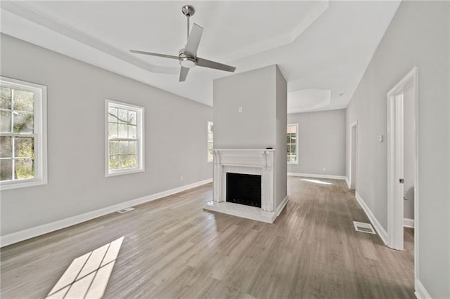 unfurnished living room with ceiling fan, a raised ceiling, and light wood-type flooring