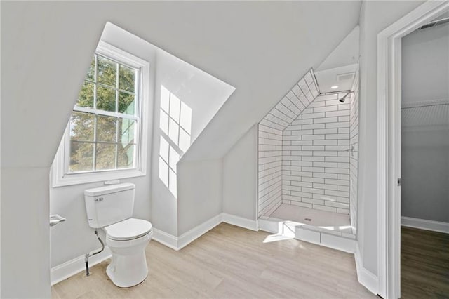 bathroom with toilet, hardwood / wood-style floors, vaulted ceiling, and a tile shower