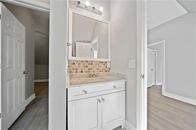 bathroom with vaulted ceiling, wood-type flooring, tasteful backsplash, and vanity