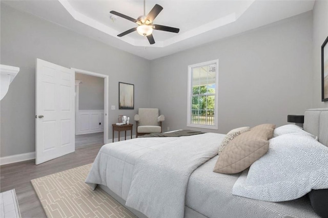 bedroom with a raised ceiling, ceiling fan, and wood-type flooring