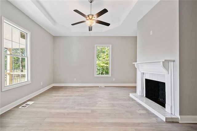 unfurnished living room featuring a raised ceiling, ceiling fan, and light hardwood / wood-style flooring