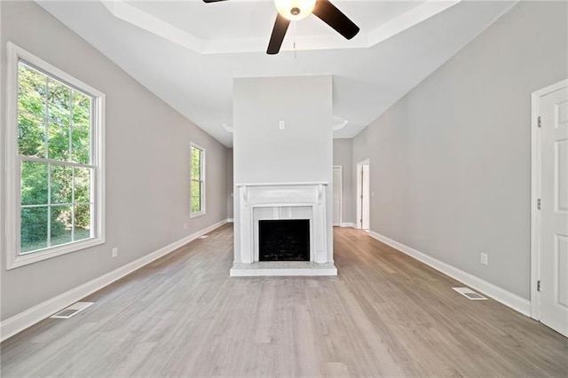 unfurnished living room with a brick fireplace, light hardwood / wood-style floors, a raised ceiling, and ceiling fan