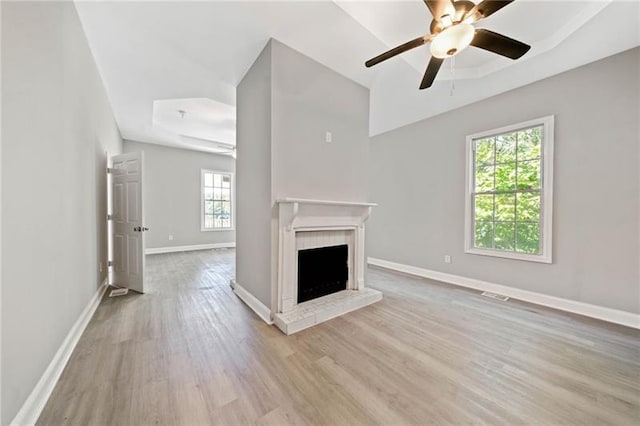 unfurnished living room with ceiling fan, a wealth of natural light, a tray ceiling, and light hardwood / wood-style flooring