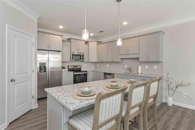 kitchen with pendant lighting, gray cabinets, appliances with stainless steel finishes, a kitchen breakfast bar, and decorative backsplash