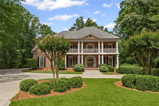 neoclassical / greek revival house with a balcony, covered porch, a front yard, and curved driveway
