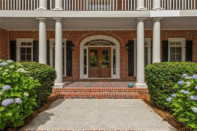 entrance to property featuring brick siding, a balcony, french doors, and covered porch