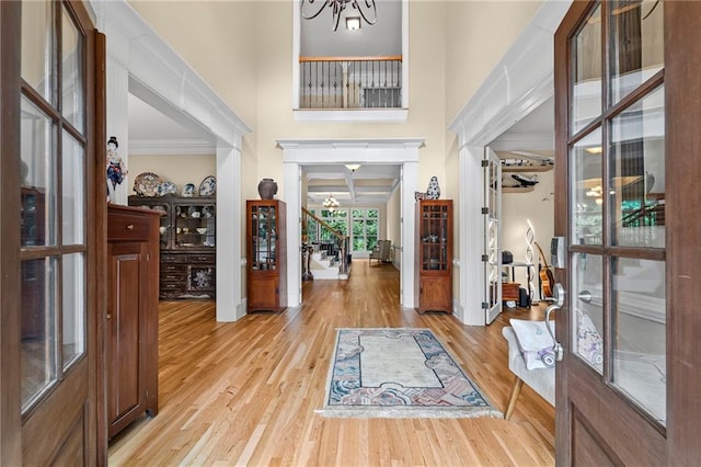 foyer featuring a chandelier, crown molding, light wood-style floors, stairs, and a towering ceiling