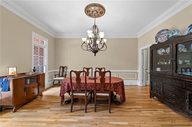 dining space with a chandelier, crown molding, light wood-style floors, and a wainscoted wall