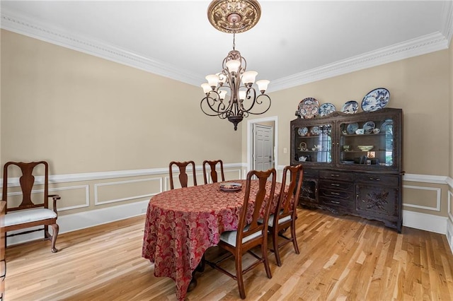 dining space with a chandelier, ornamental molding, light wood-type flooring, wainscoting, and a decorative wall