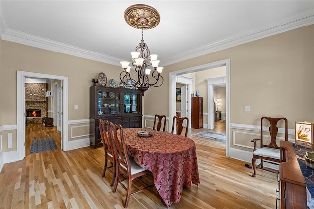 dining space with crown molding, a chandelier, light wood-style floors, a decorative wall, and wainscoting