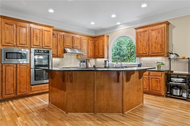 kitchen featuring appliances with stainless steel finishes, under cabinet range hood, dark countertops, a kitchen island, and light wood-type flooring
