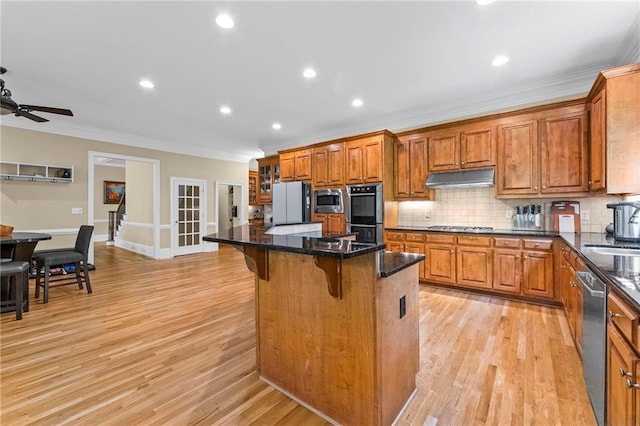 kitchen with under cabinet range hood, appliances with stainless steel finishes, brown cabinets, crown molding, and a breakfast bar