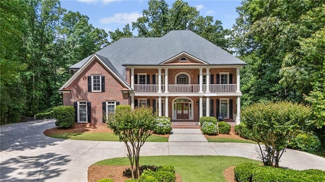 greek revival inspired property featuring a balcony, a porch, curved driveway, and a front lawn